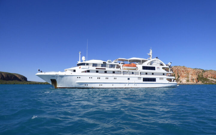Port side exterior of Coral Adventurer small white expedition ship with 5 decks cruising on a sunny day in Australia.