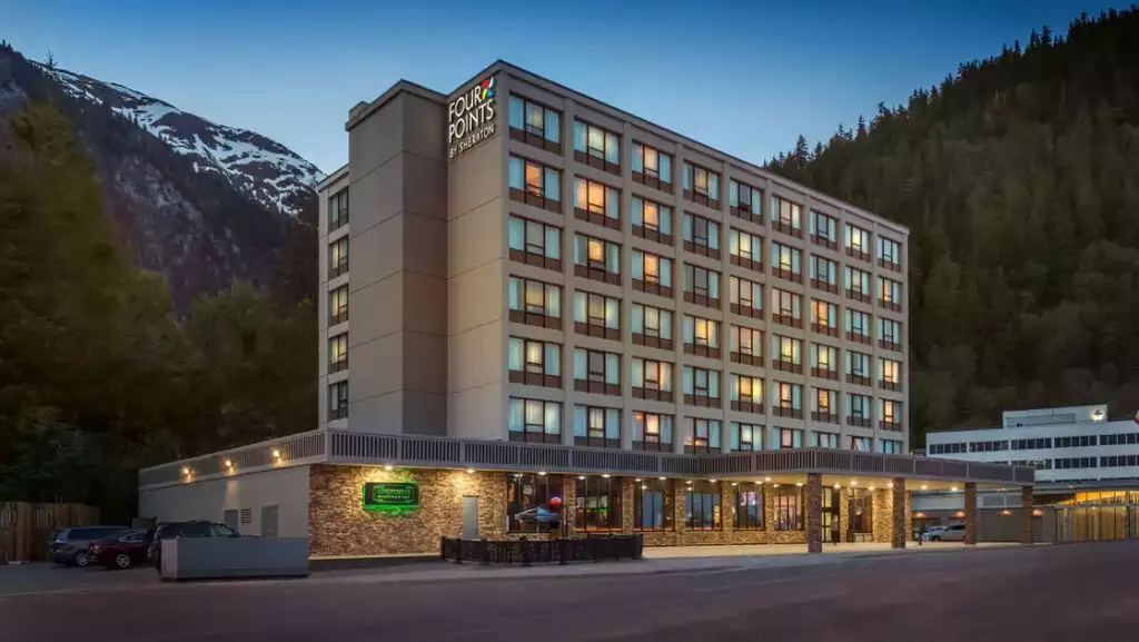 Four Points by Sheraton rectangular beige hotel with 7 floors & ground floor Irish pub restaurant at dusk with mountains behind.