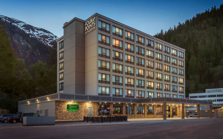 Four Points by Sheraton rectangular beige hotel with 7 floors & ground floor Irish pub restaurant at dusk with mountains behind.