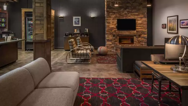 Lobby lounge of Four Points by Sheraton Juneau hotel with brick fireplace, distressed wood decor, beige & brown couches & table.