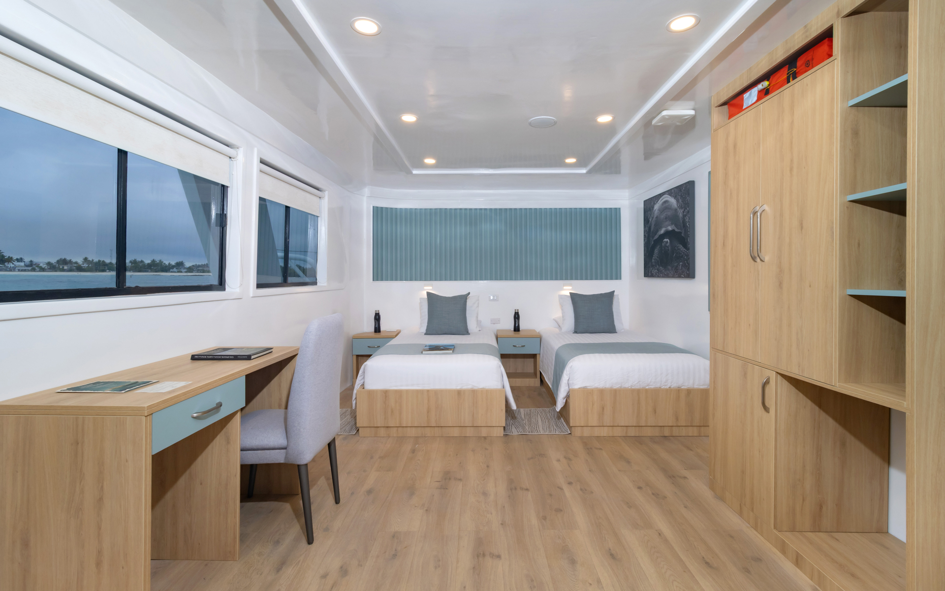 Upper Deck Suite aboard Galapagos Sea Star room with two twin beds and desk area. Tans, greys and blues for design