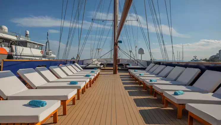 Big open sun deck with rows of plush white chaise loungers below the rigging & blue sky on the Galileo cruise ship.