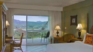 Room with bed, armchair, desk, chair and balcony with hammock, chair and forest views at Gamboa Rainforest Resort in Panama