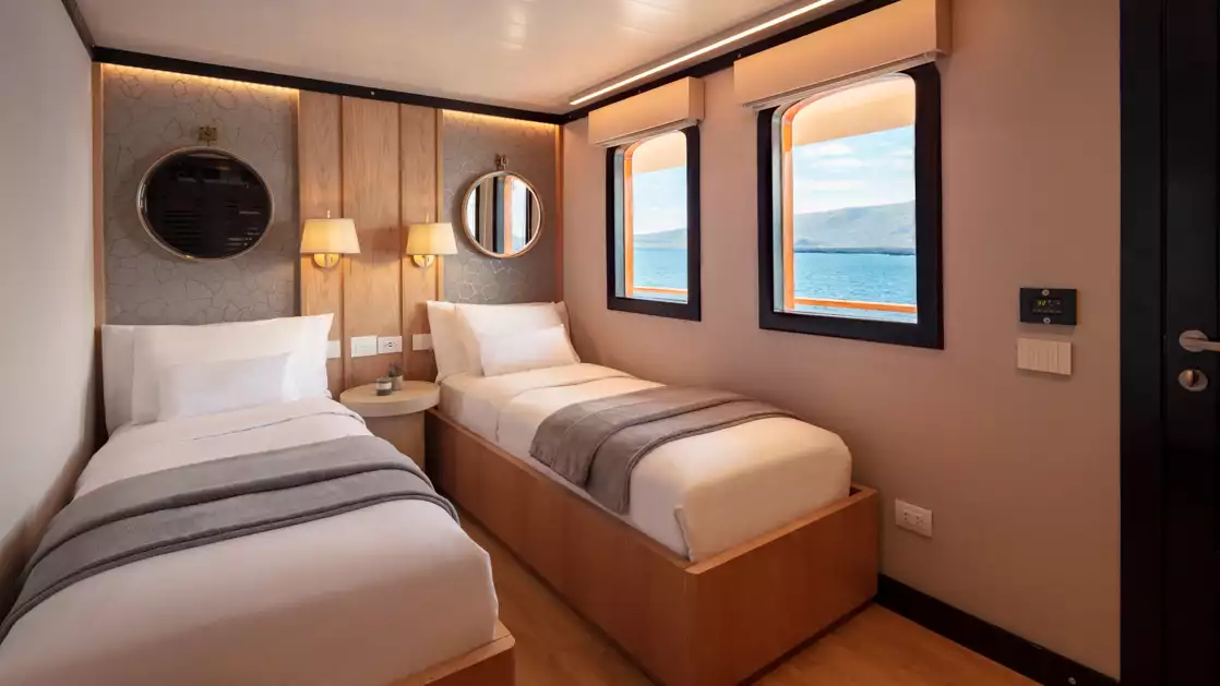 Historic wooden Twin Suite with white sheets with a shared bedside table and two large windows looking out at the ocean