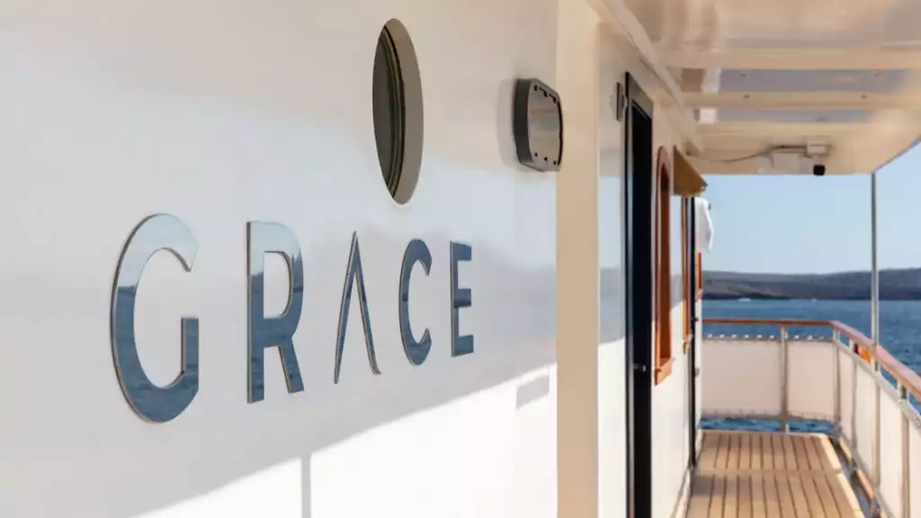 The name of the ship Grace in metallic letters below a porthole featuring the wooden planked deck and the canvas covered rail