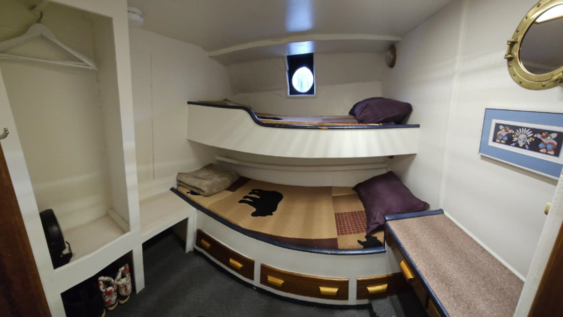 Cabin on M/V Discovery Alaska yacht with white wooden built-in bunkbeds, mirror, framed art, small closet & porthole.