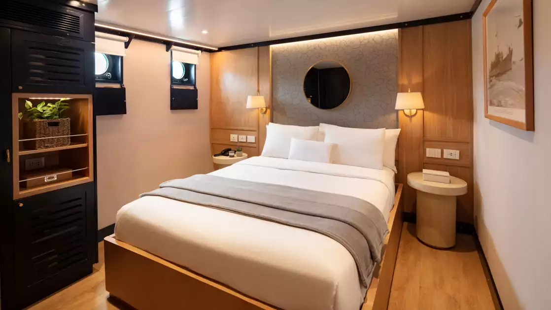 Large bed with white bedding and flanked by nightstands featuring two portholes and a large historic photograph of the Grace