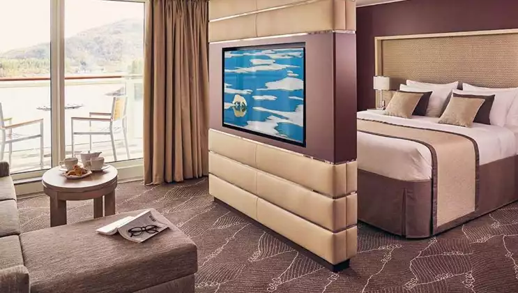 Balcony Suite with double bed, couch, desk, chair, and private balcony with table and chairs aboard National Geographic Endurance polar expedition ship.