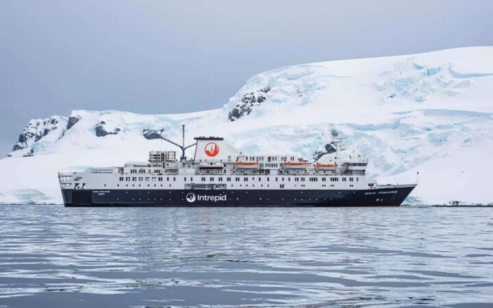 The Ocean Endeavour ship floats in front of a snow white mountain landscape in Antarctica on an overcast day.