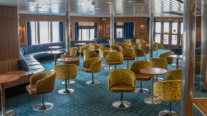 a lounge room with blue carpet and green chairs aboard Ocean Endeavour small ship