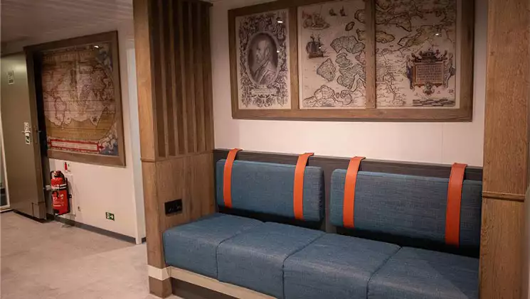 Renovated reception area on Ortelius ship with classic polar maps, modern blue bench seating, wood accents & beige floor.