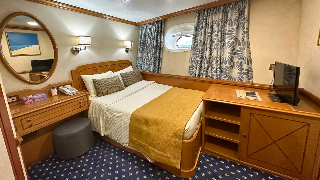Bed with towel shaped like a swan and small porthole, mirror and curtains aboard Panorama II