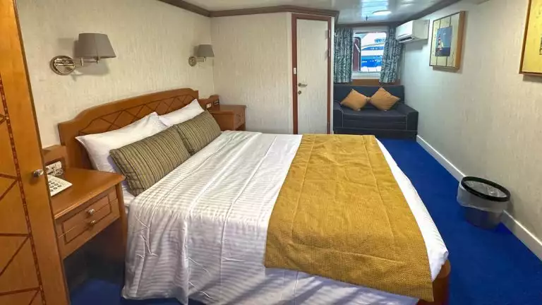 Double bed with mirror and wine and snacks on bed side table with small window aboard Panorama II