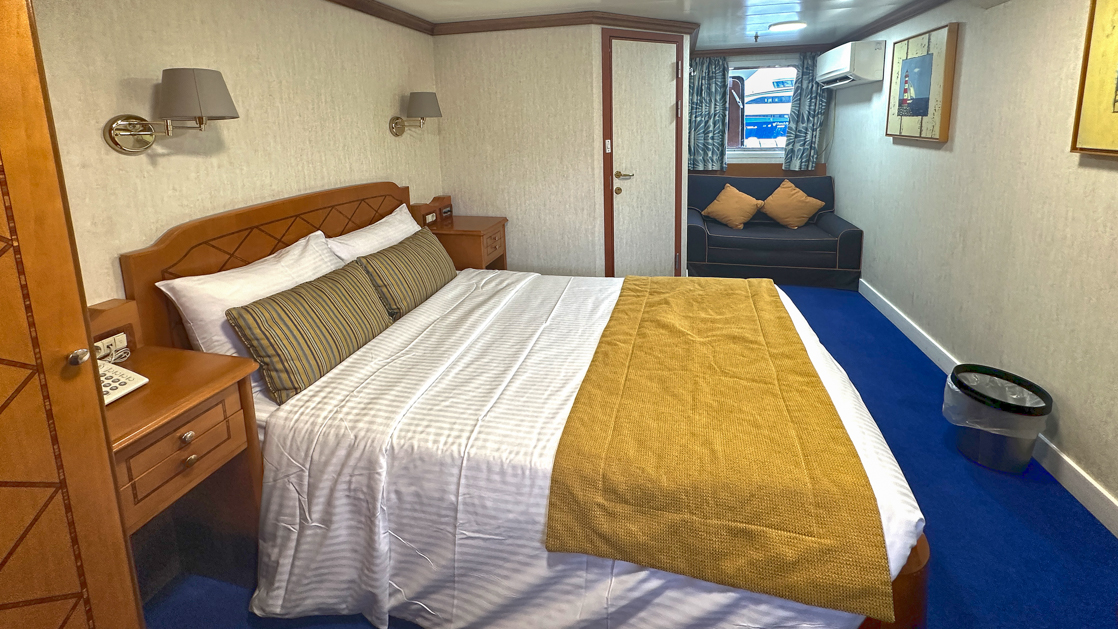 Double bed with mirror and wine and snacks on bed side table with small window aboard Panorama II