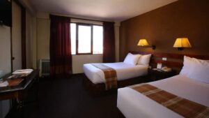 A room with two queen-sized beds, fresh linens, lamps, and a large window at the Casa Andina Classic Cusco San Blas, a quiet and cozy hotel in Cusco, Peru