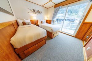 Admiral stateroom with large bed with pillows on it and a large window behind it aboard the Safari Quest pacific northwest small ship