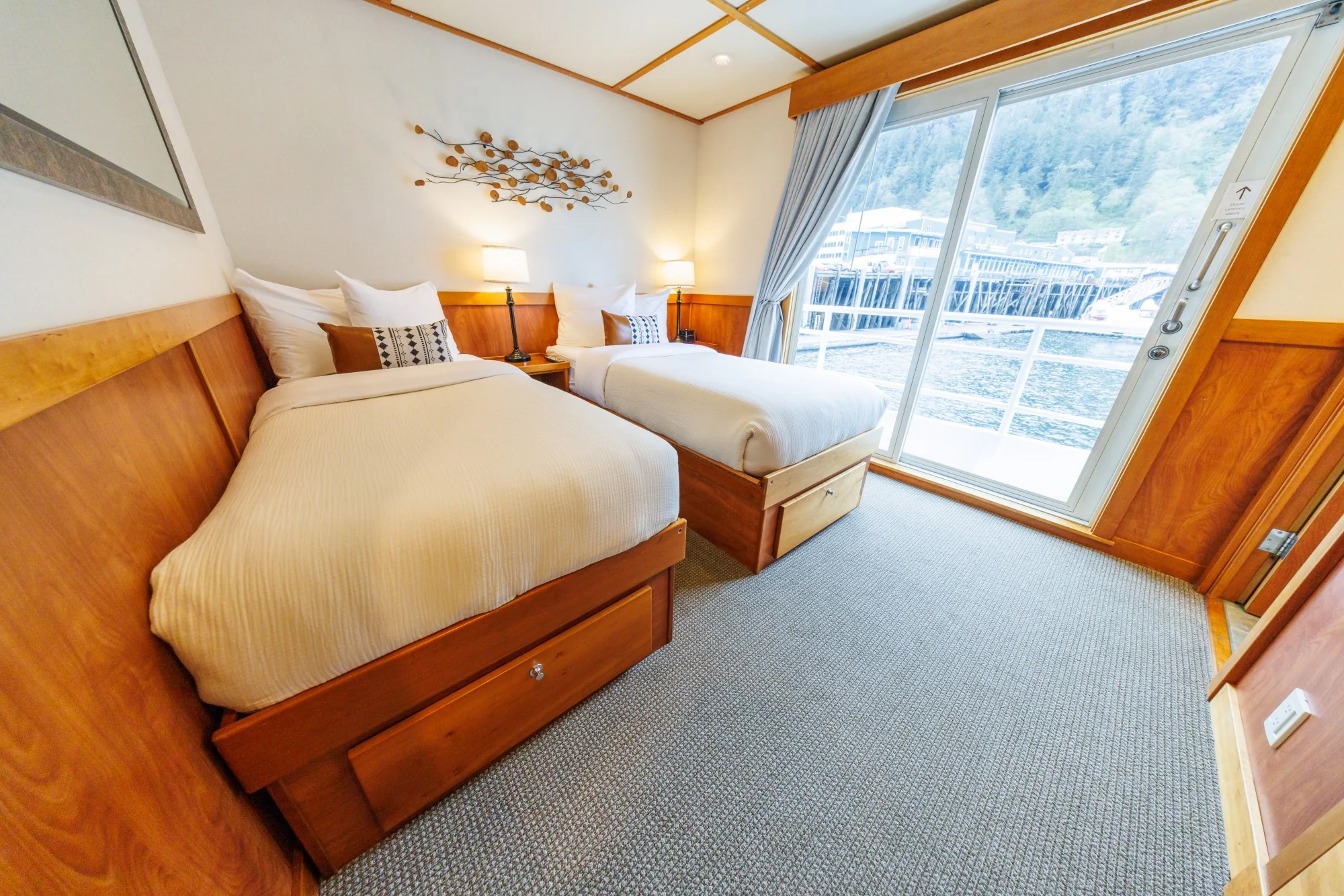 Admiral stateroom with large bed with pillows on it and a large window behind it aboard the Safari Quest pacific northwest small ship