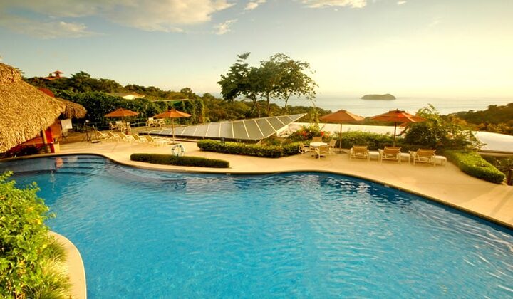 Solar panels are installed next to a pool, with a patio, umbrellas, lounge chairs, and an ocean view at Si Como No Resort on Costa Rica's Pacific Coast