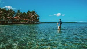 A man fishing while standing in the water in front of the Turneffe Flats lodge.