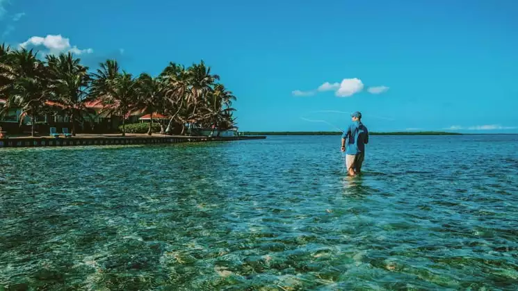 A man fishing while standing in the water in front of the Turneffe Flats lodge.