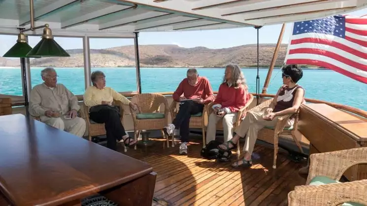 Travelers relaxing on the back deck of the westward in wicker chairs and american flag.