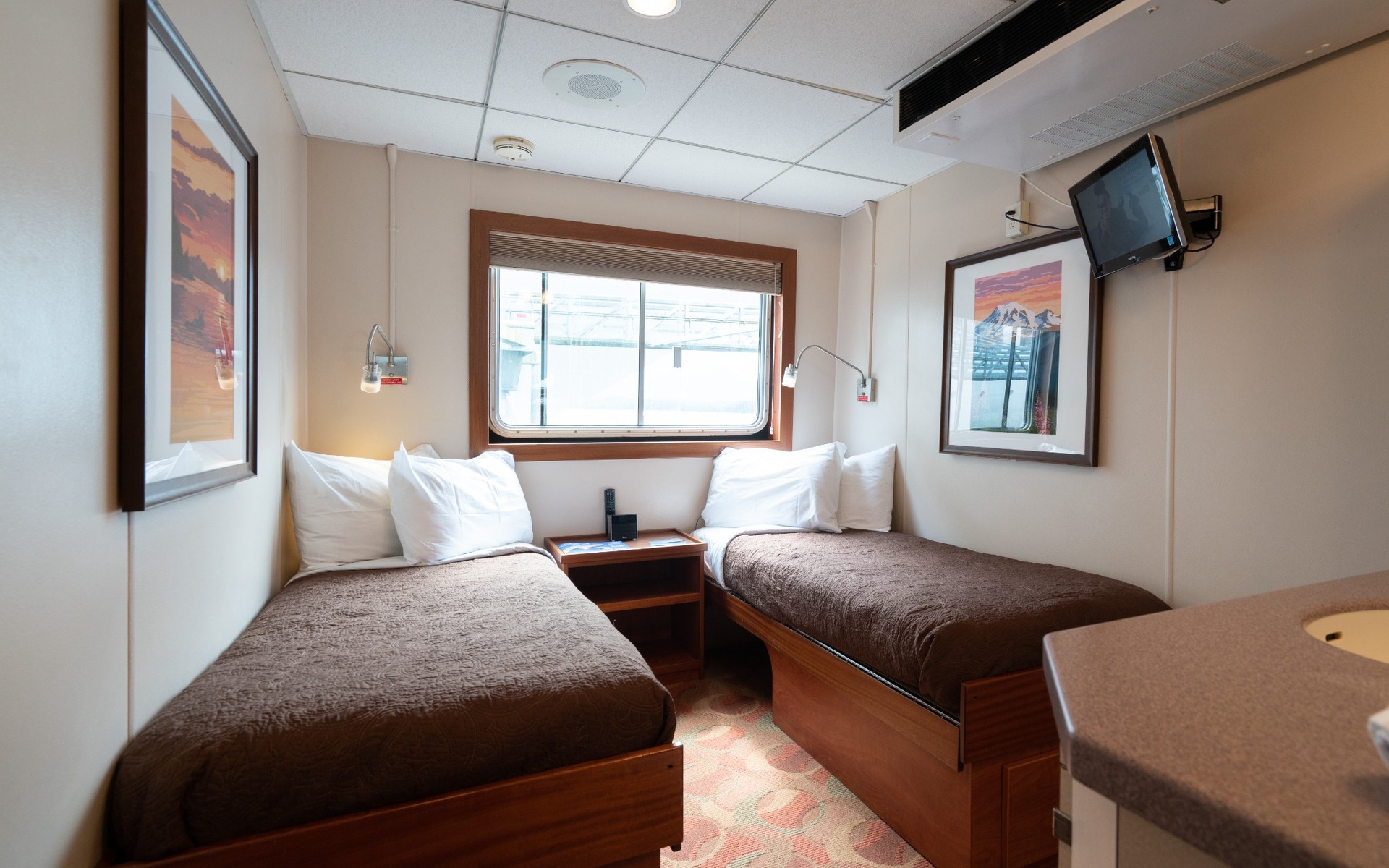 Pathfinder cabin with two single beds wrapped in brown comforters and a view window aboard Wilderness Explorer.