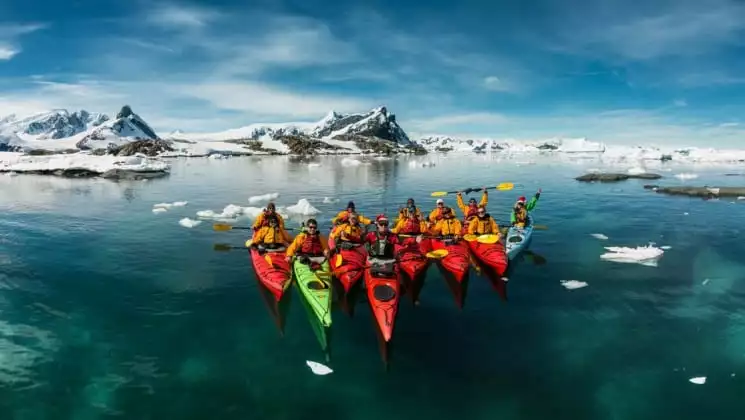 A group of sea kayaks pose in the ocean in front of icebergs in antarctica