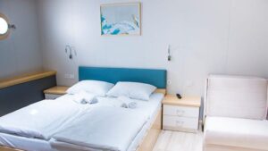 Fantazija stateroom with double bed, chair, nightstand and porthole.