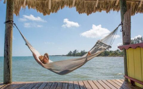 A traveler relaxing in a hammock on a dock with a grass shade.