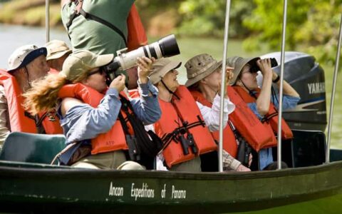 a small skiff boat full of people pointing and taking photographs goes down the river during the best of panama land tour