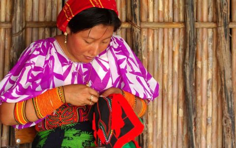 an indigenous woman in a bright top weaving in front of a thatched wooden wall on the best of panama land tour