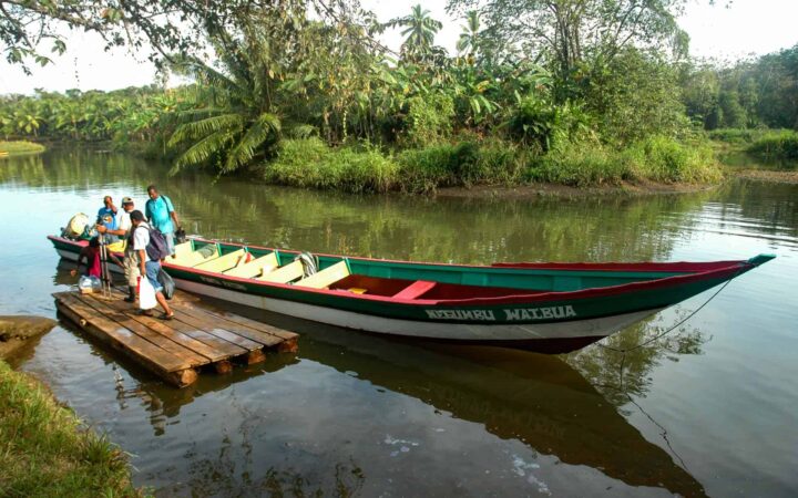 a large canoe docked on a still river with foliage in the background and adventure travelers get off of it during the best of panama land tour