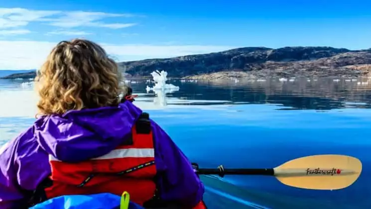 Up close of a female kayaker pausing to admire the landscape of greenland with calm waters, blue skies, and icebergs passing by