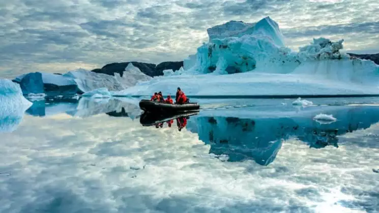Skiff excursion with group surrounded by uniquely shaped icebergs and reflections on the still water