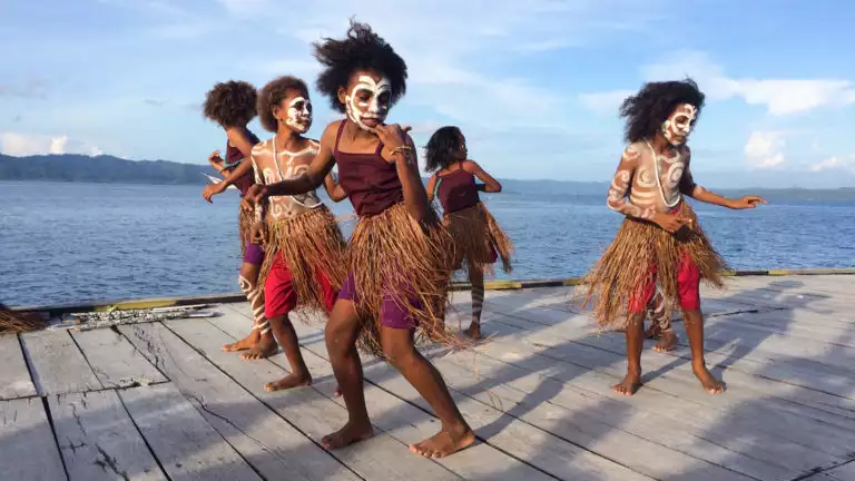 children with indigenous outfits and face paint dance on a dock on a sunny day in indonesia