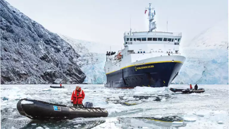 National Geographic small ship in front of glacier and two skiffs in front surrounded by ice in Garibaldi Fjord of Tierra Del Fuego Patagonia