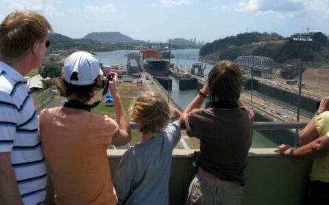 a family stands above the miraflores locks in panama on a sunny day pointing and taking pictures