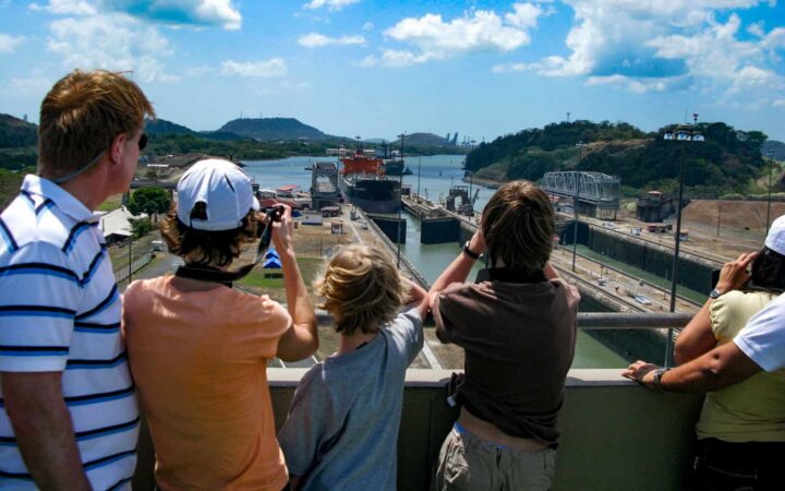 father and three kids overlook a small ship crossing the miraflores lock in the panama canal