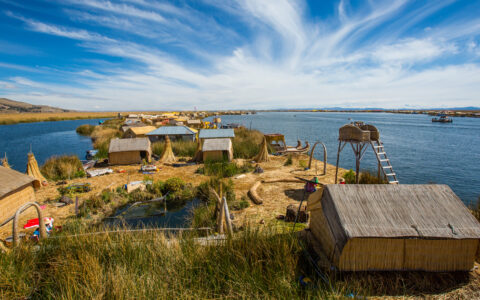 looking down a strip of dry land with hugs and various structures on it with the water of lake titicaca peru on either side