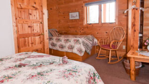 A room at Annie Mae Lodge with wood walls and a twin and queen, rocking chair and table.