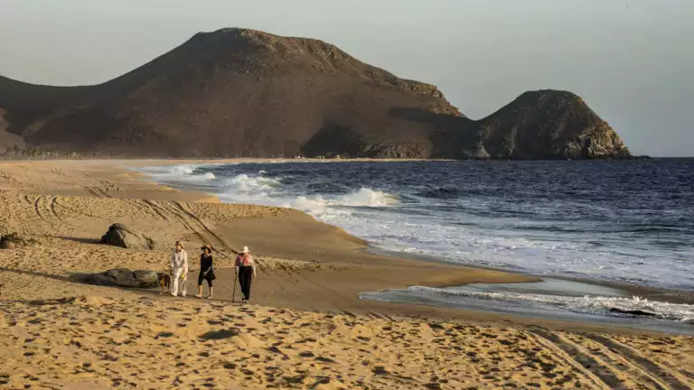 three people walking along the ocean on a sandy beach as the sun is starting to go down