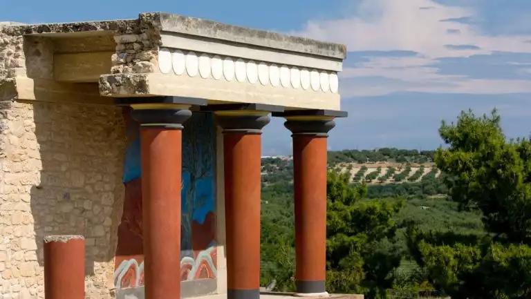 Red Greek pillars support an ancient stone building shown on a sunny day during a Greece cruise.