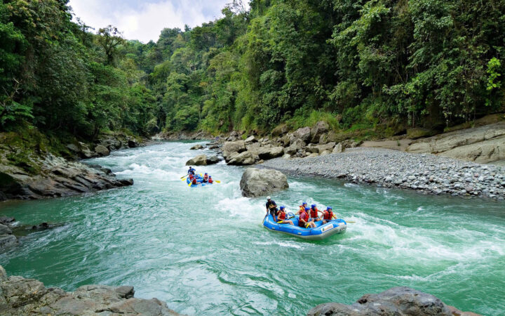 Two rafts of Costa Rica travelers floating down a turquoise river with rocks and green trees lining the river.