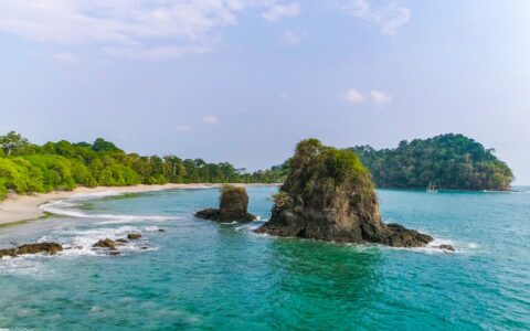 Manuel Antonio beach in Costa Rica, with white sand, bright green forest, turquoise water & lots of sunshine.