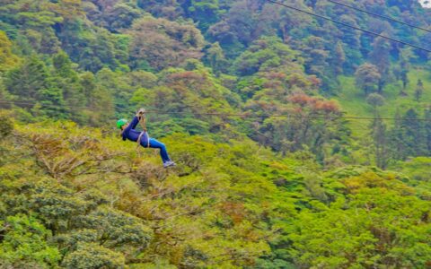 Girl zip lines above bright green rainforest on a sunny day during the Costa Rica Family Adventure.