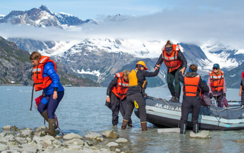 Alaska travelers exit a skiff boat onto a rocky beach on the Glacier Bay National Park, Haines & Pelican Cruise.