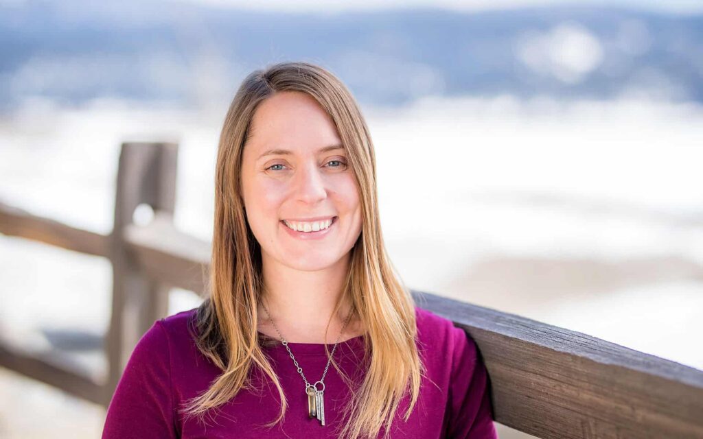 adventuresmith explorations financial controller jennifer yordy wearing a pink sweater smiling and standing against a fence with snow in the background