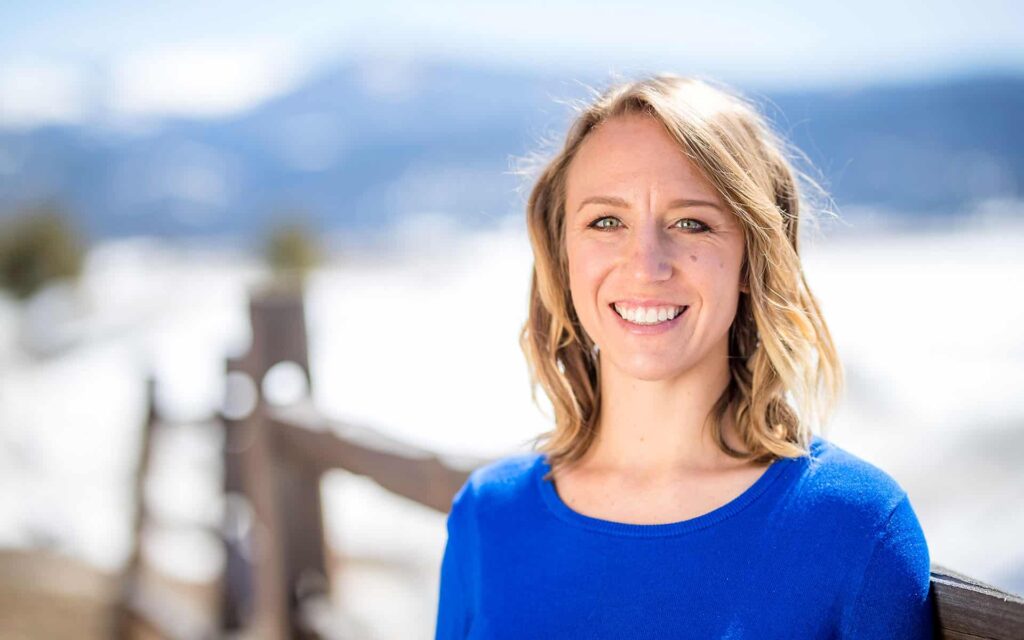 adventuresmith explorations adventure coordinator kelly gorrell wearing a bright blue shirt and smiling in front of a snowy landscape