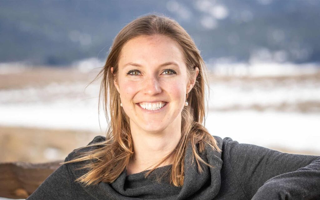 adventuresmith explorations office manager lauren pilholski stands against a fence smiling with a snowy field behind her