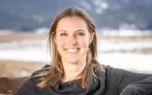 adventuresmith explorations office manager lauren pilholski stands against a fence smiling with a snowy field behind her